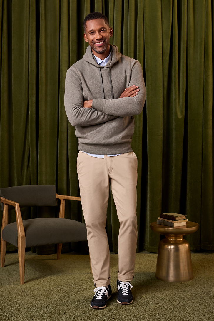 Man standing with arms crossed in a room with green curtains and a chair.