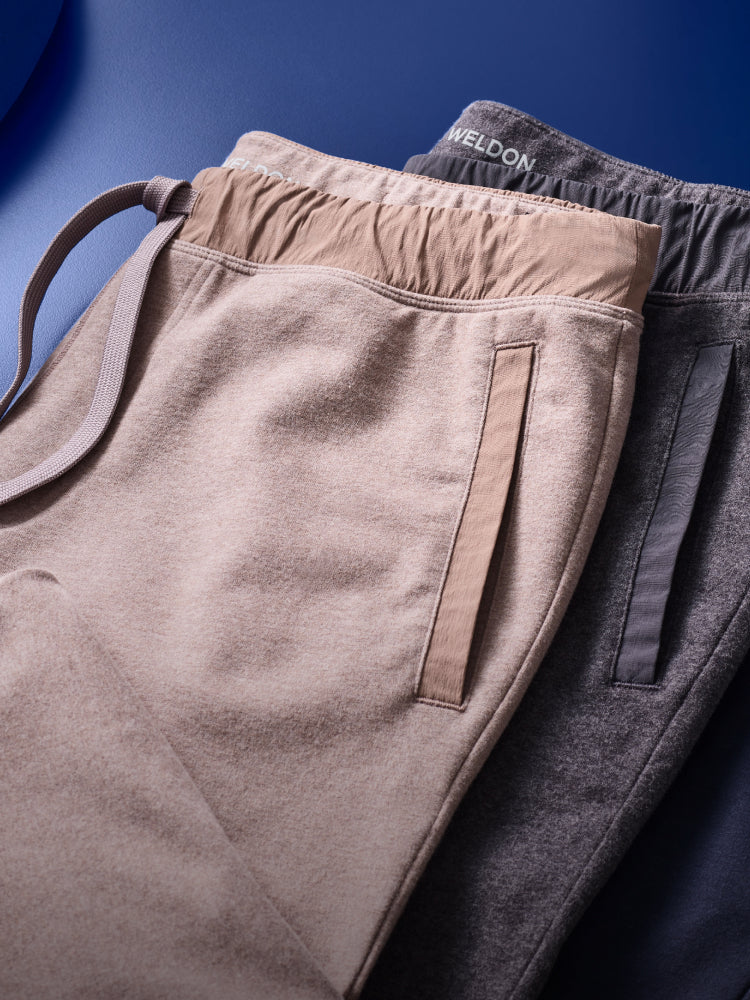 two ACE sweatpants in cream and grey lay on a blue backdrop