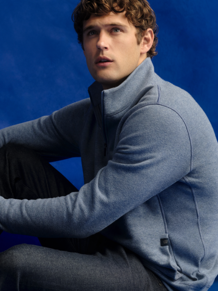 Man sitting on the floor with a blue backdrop. He is wearing Mack Weldon jean and a blue ACE half zip