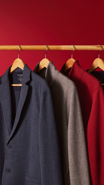 Three coats hanging on wooden hangers against a red wall.