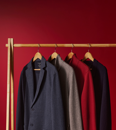 Four coats hanging on a rack against a red wall