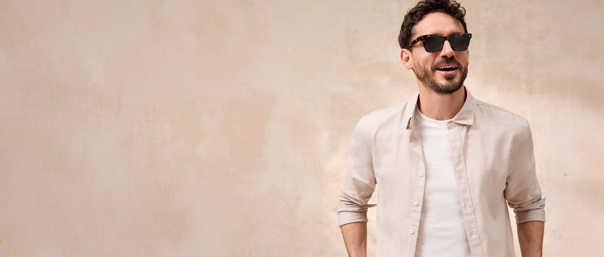 Man wearing sunglasses and a light-colored shirt against a beige background