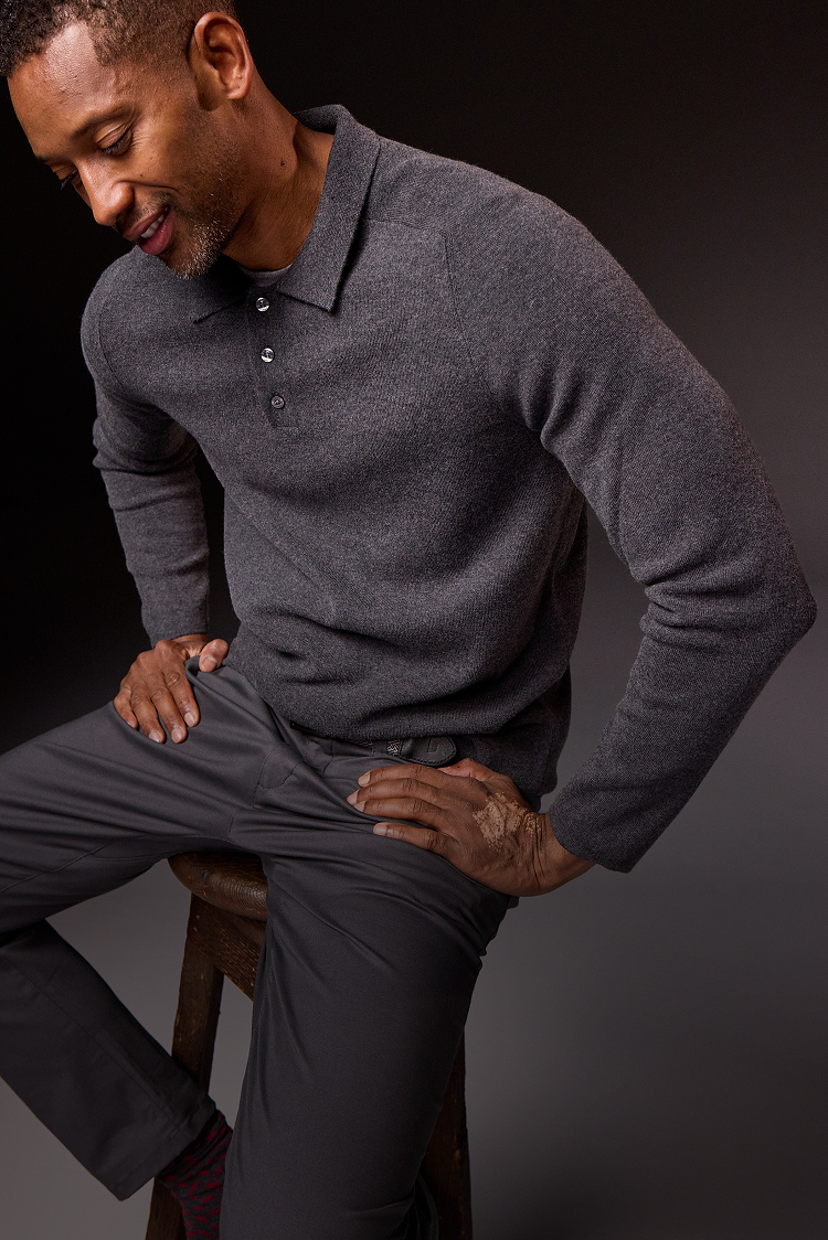 Man wearing a gray long-sleeve polo shirt and pants against a dark background