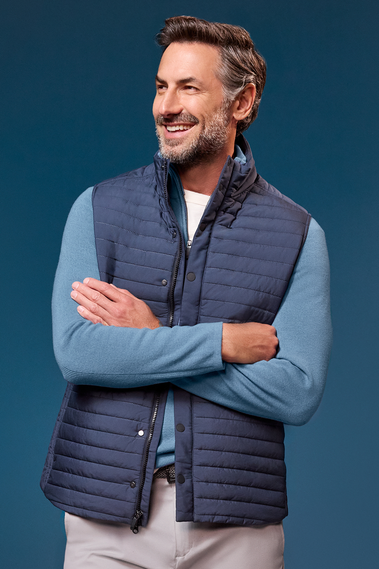 Man wearing a blue quilted vest over a blue shirt against a dark blue background