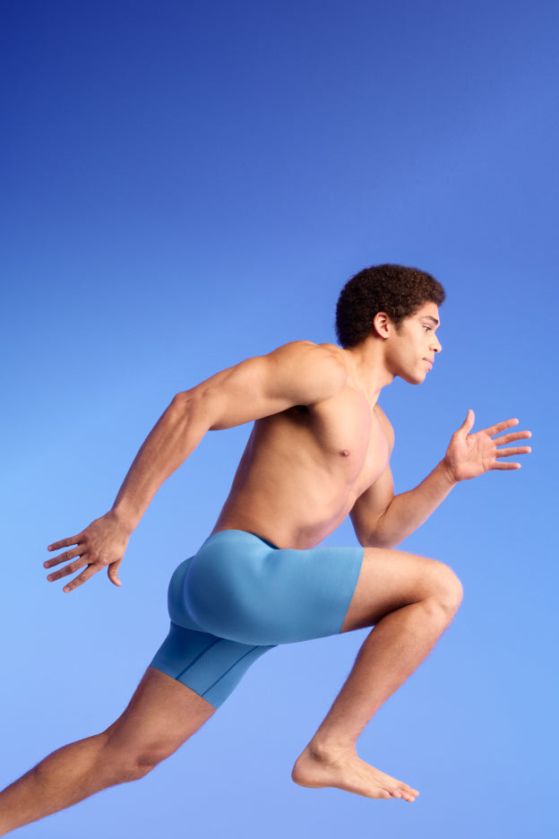 Man in blue athletic shorts running against a blue background