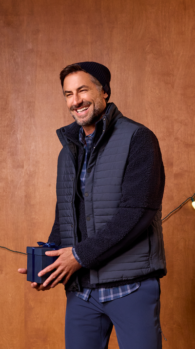 Man wearing a dark blue vest holding a small blue box against a wooden background