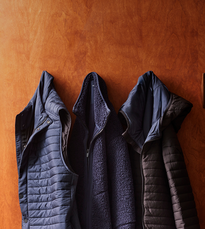 Three blue quilted jackets hanging against a brown wall.