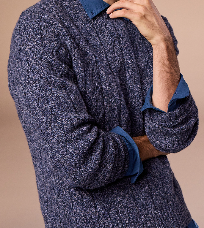Close-up of a person wearing a blue cable knit sweater with a blurred background
