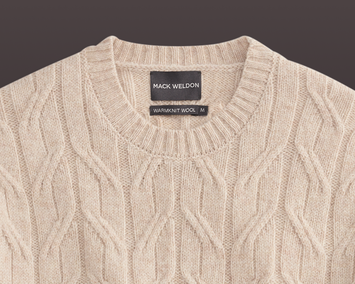 Beige cable knit sweater with Mack Weldon label on a dark background