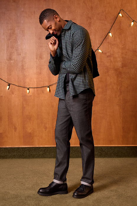 Man adjusting his jacket against a wooden paneled wall with string lights.