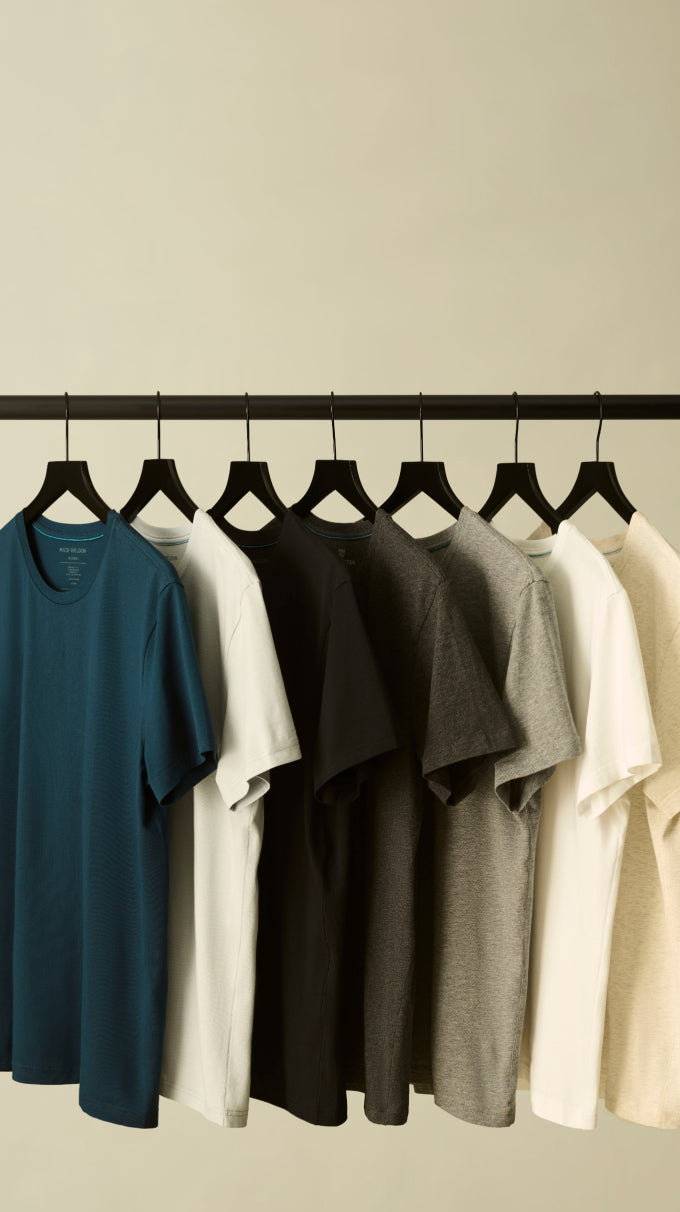 A row of Mack Weldon T-shirts hanging on black hangers 