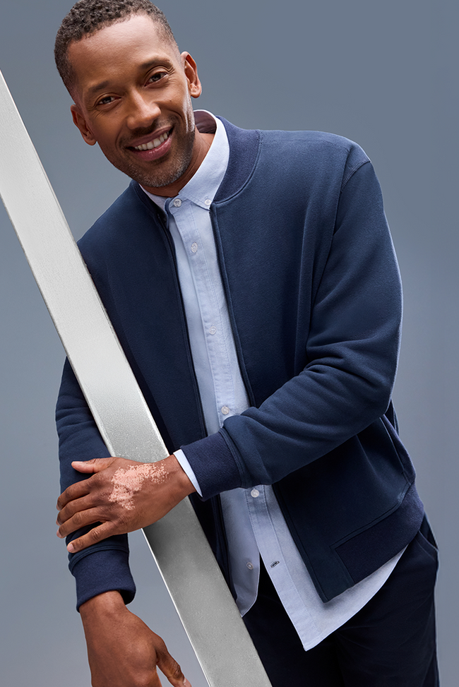 Man wearing a navy blue jacket over a light blue shirt against a gray background