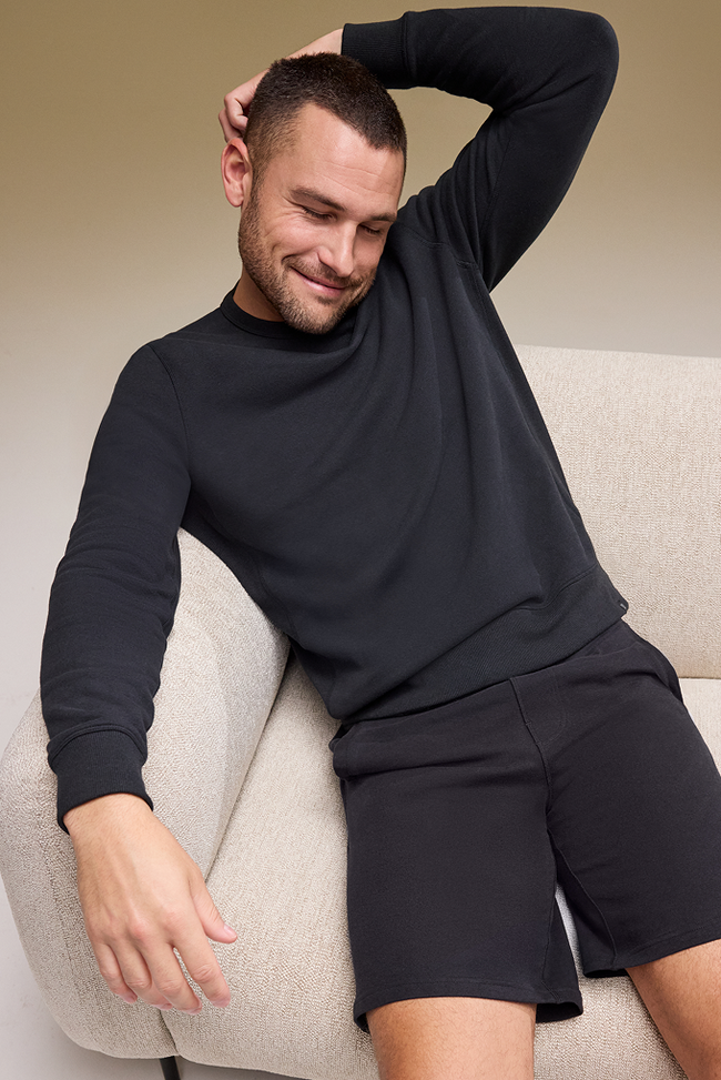 Man wearing a black outfit sitting on a beige chair.
