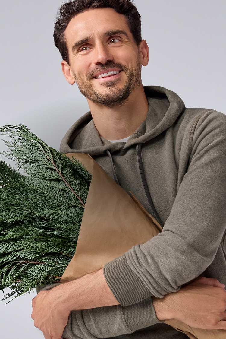 Man wearing a brown apron holding greenery against a light gray background