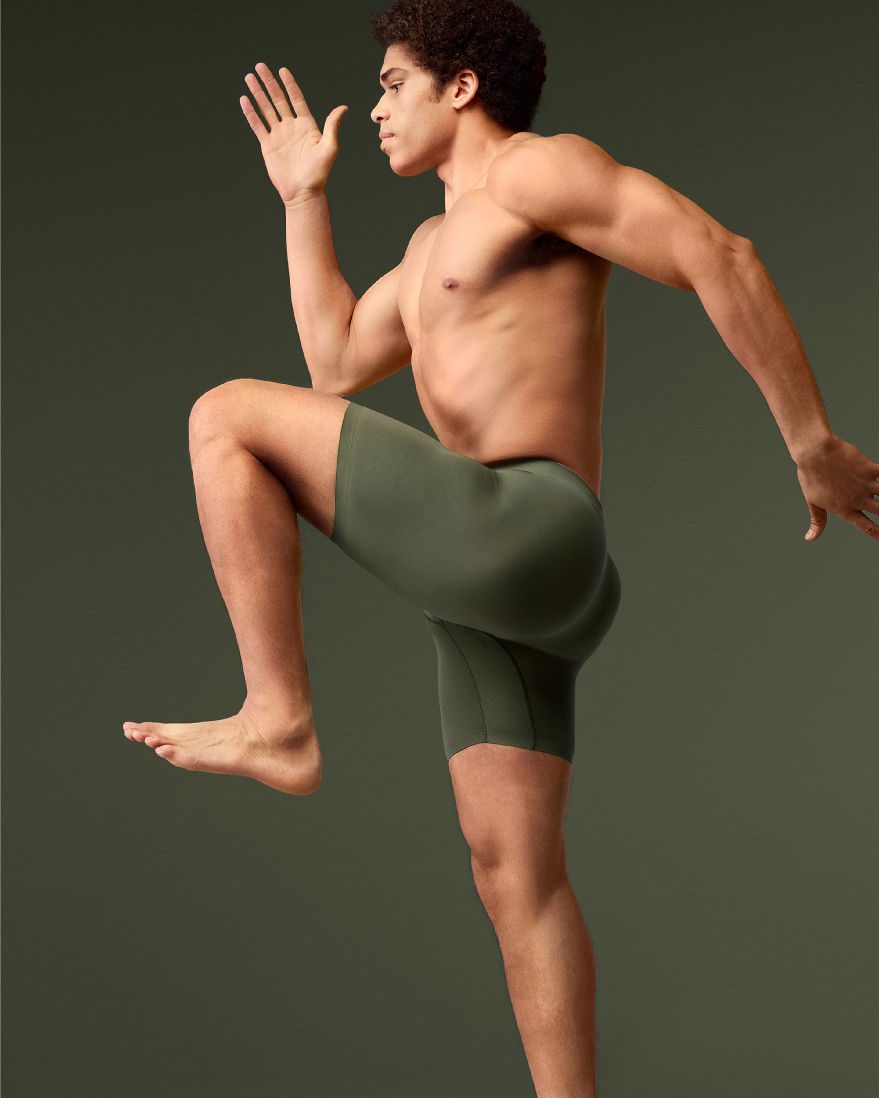 Image of man in a running position wearing a dark green Stealth Pro boxer brief with a dark green backdrop