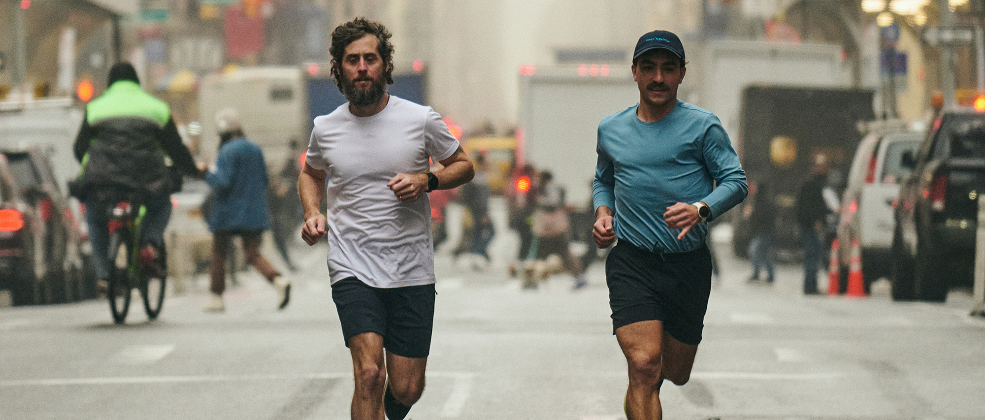 Two men run in the middle of wide busy street