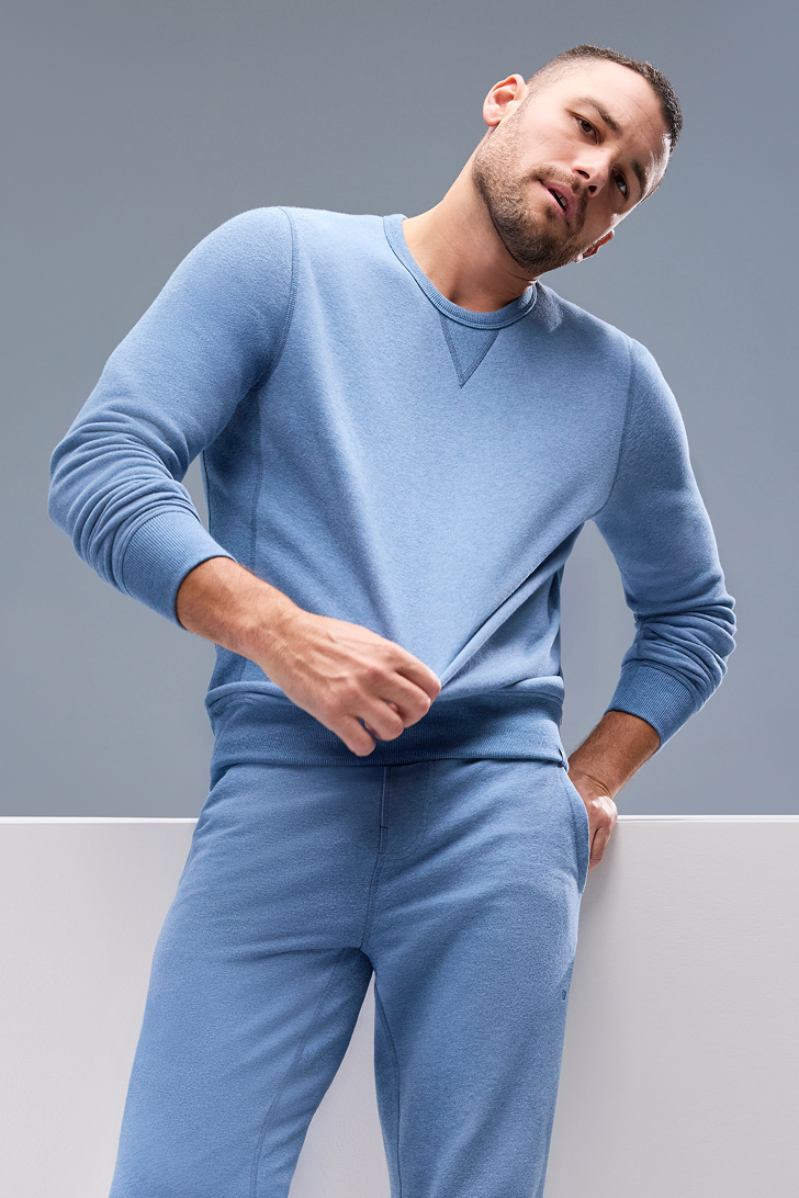 Man wearing a blue sweater and pants against a gray background