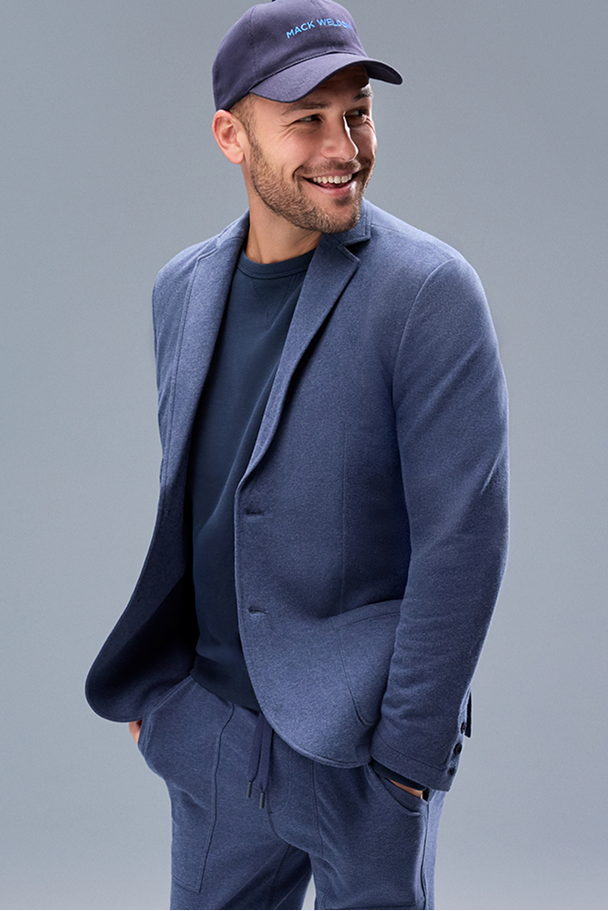 Man wearing a blue blazer and cap against a gray background