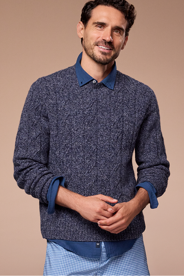 Man wearing a blue patterned sweater with a matching shirt collar against a beige background