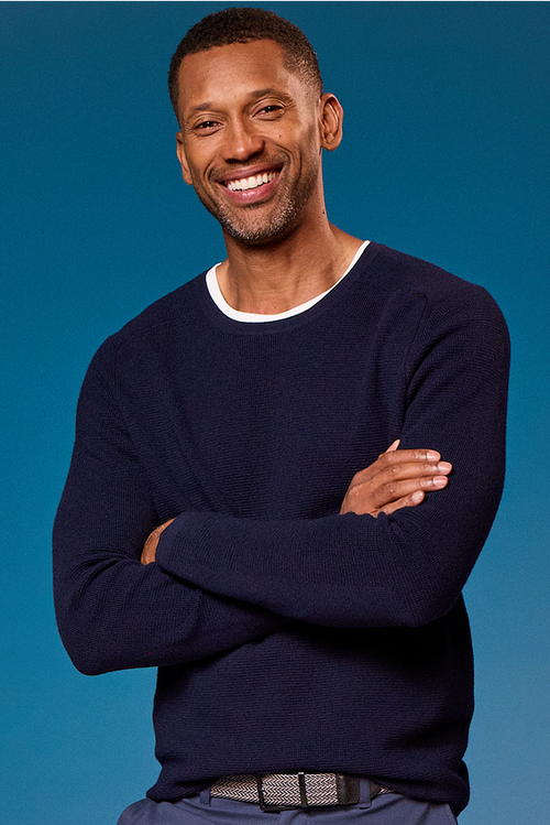 Man wearing a navy sweater with arms crossed against a blue background