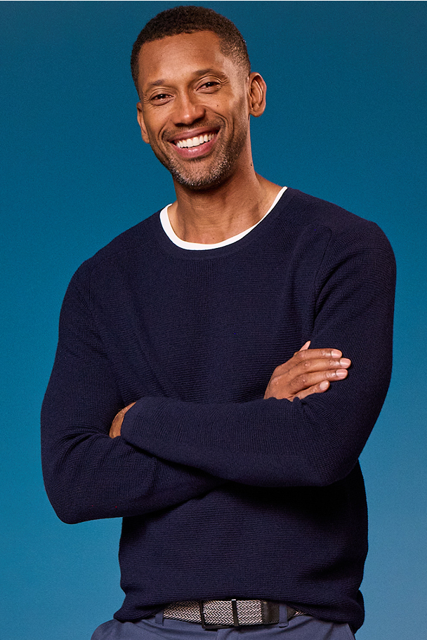 Man wearing a navy sweater with arms crossed against a blue background