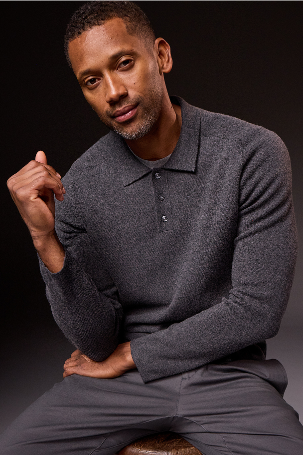 Man wearing a dark gray long-sleeve shirt sitting on a stool against a black background