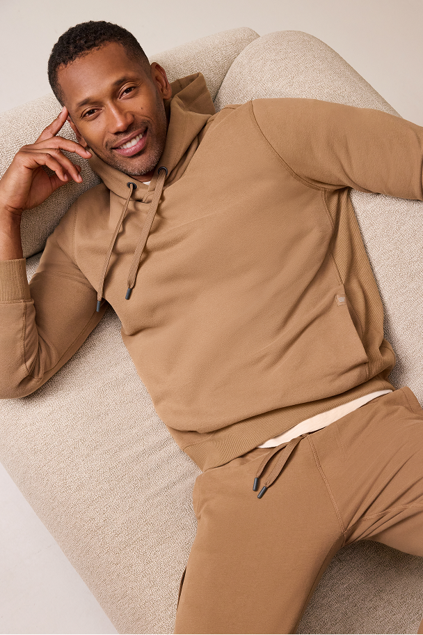 Man wearing a beige tracksuit sitting on a beige couch.